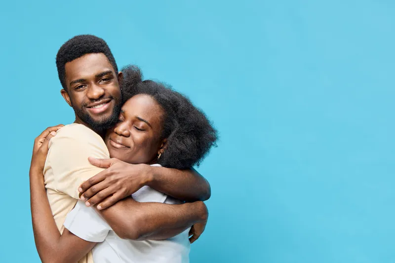Happy Black couple embracing against a blue background, showcasing love and connection, perfect for themes of relationships, affection, and joy in diverse cultures