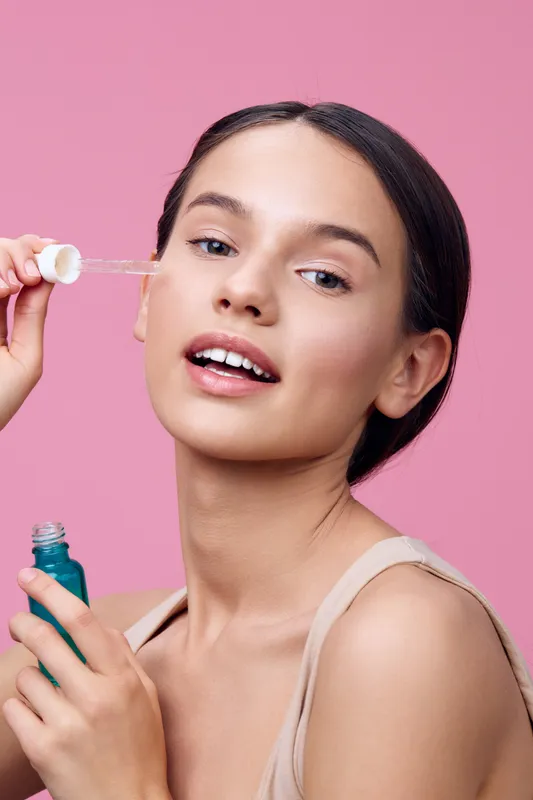 Young woman applying facial serum on her face, showcasing healthy skin, beauty routine, on a pink background Perfect for skincare and beauty concepts