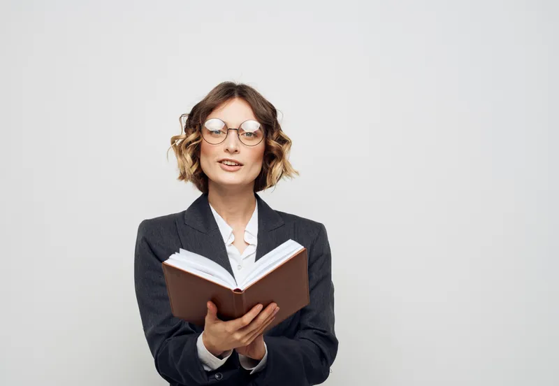 Женщина в классическом костюме с открытой книгой и очками на лице, обрезанный вид