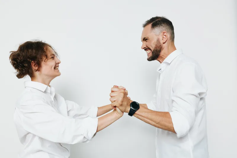 Two professional men in business attire share a confident moment, celebrating teamwork with a warm smile, a firm handshake, and clear eye contact. The isolated colored backdrop emphasizes focus,
