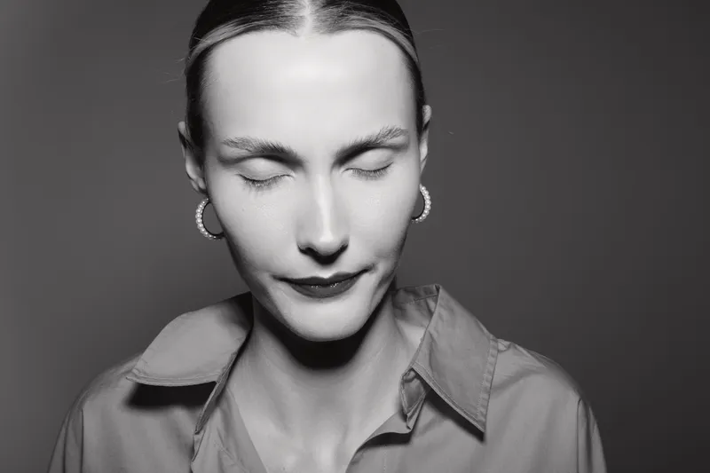 Closeup of a fair skinned Caucasian woman with closed eyes and pearl earrings in black and white studio portrait.