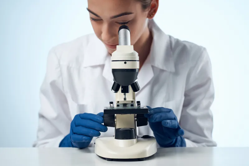 Женщина-химик работает в лаборатории с микроскопом, занимаясь исследованиями в области биотехнологий