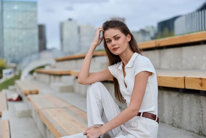 young woman in white casual outfit sitting on wooden urban stairs with thoughtful expression in city environment