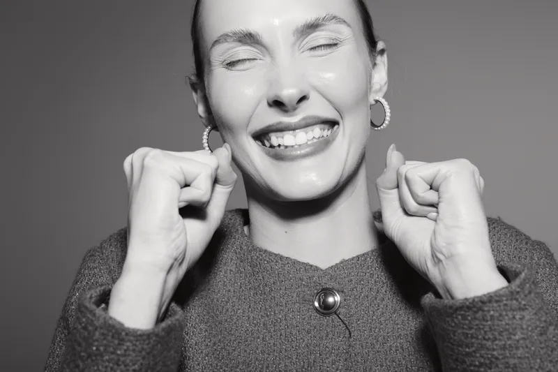 Happy caucasian woman with light skin laughs joyfully with eyes closed and clenched fists. Studio portrait in black and white. Concept of positive emotions and celebration.
