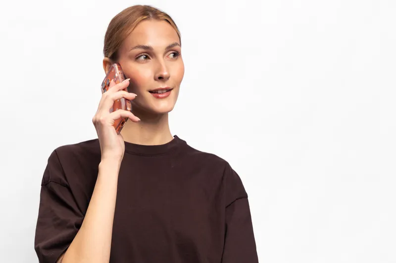 Young woman with light hair wearing dark shirt talks on smartphone looking to side isolated on white background. Concept of communication, technology, lifestyle, and casual conversation.