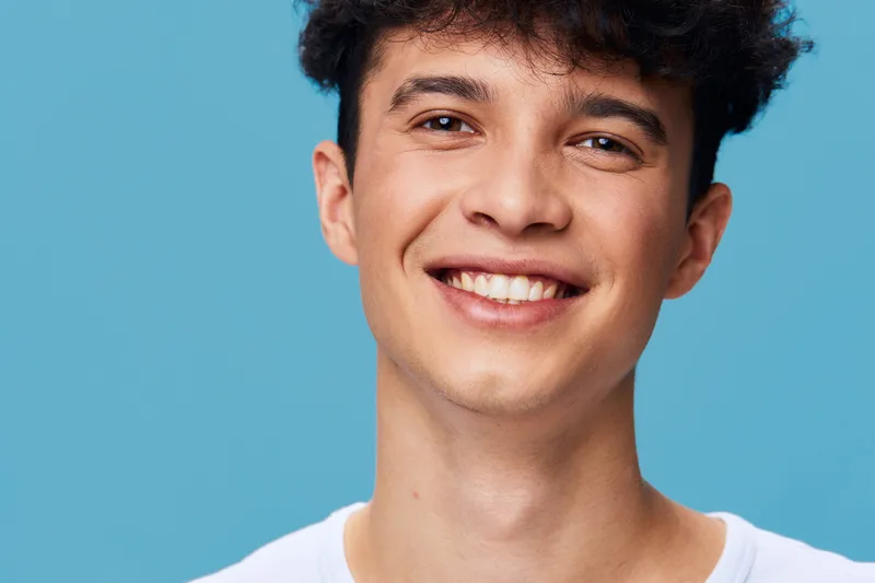 smiling man with curly hair wearing a white shirt on a bright blue background, happy expression, youth, casual style, positive mood, isolated portrait