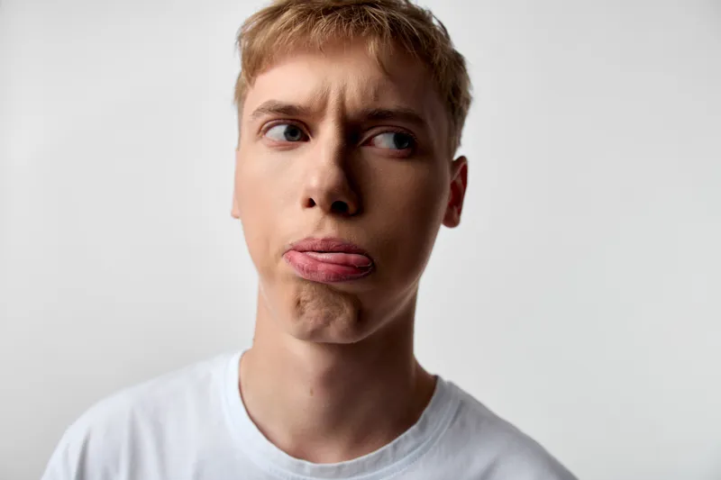 Close-up of a man with a playful tongue out, a silly expression and casual white shirt, conveying humorous mood and lighthearted vibe for reaction shots and playful branding concepts