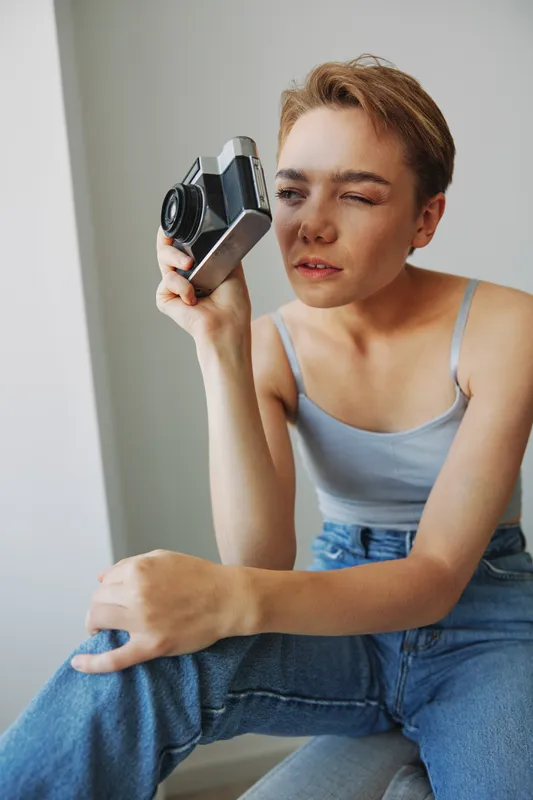 Женщина-фотограф снимает в студии на старую плёночную камеру, сидя на диване дома