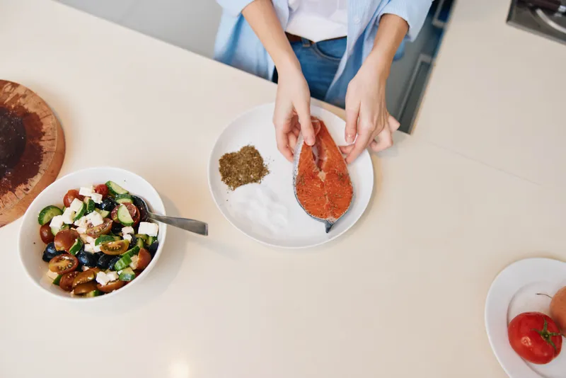 Женщина готовит здоровую еду на кухонной стойке, используя свежие овощи и нежирное мясо