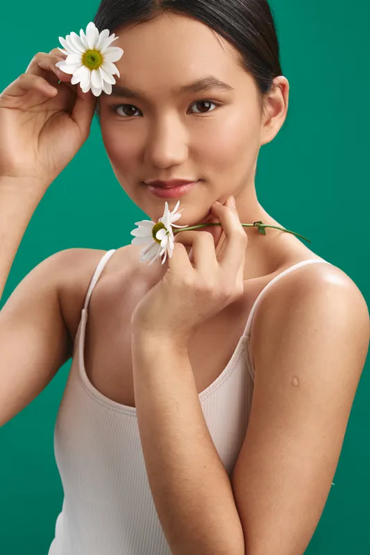 asian woman posing with flowers in a studio portrait, gentle expression and soft lighting against a vibrant green backdrop, conveying elegance and natural beauty.