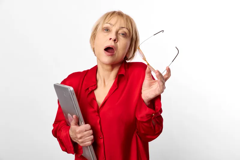Woman surprised with tablet in studio, wearing red shirt, holding glasses frame, open mouth expression, looking at camera, clean white background, soft light, bright studio light overhead