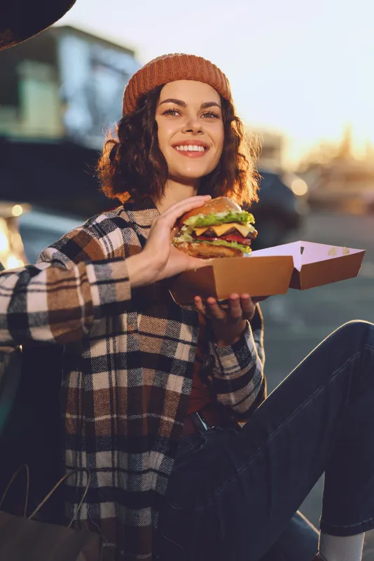woman burger smile outdoor urban beanie takeout golden enjoying a candid lifestyle moment at golden hour glow, authenticity and emotional storytelling of mindful living in a modern city street