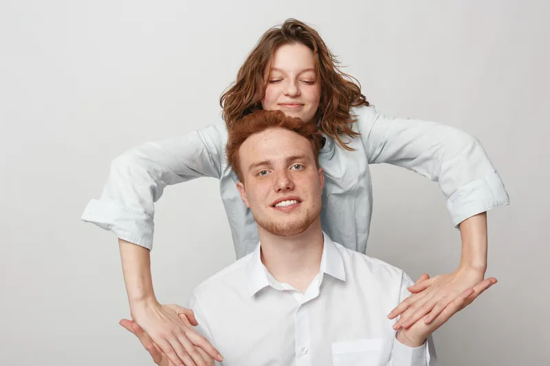 Happy young couple in white shirts posing together on light background. Smiling man and woman show playful mood and close relationship in casual studio portrait.