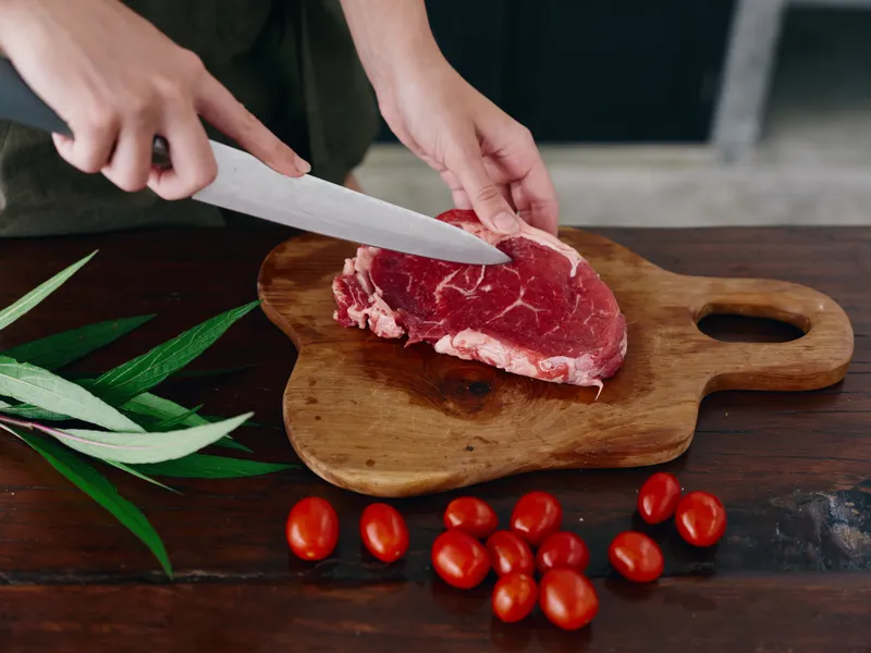 Женщина с ножом в руке нарезает свежее мясо стейка для жарки на кухне