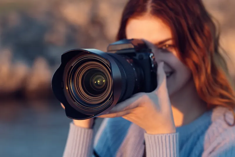 Симпатичная женщина с фотоаппаратом на природе в горах, на заднем плане река