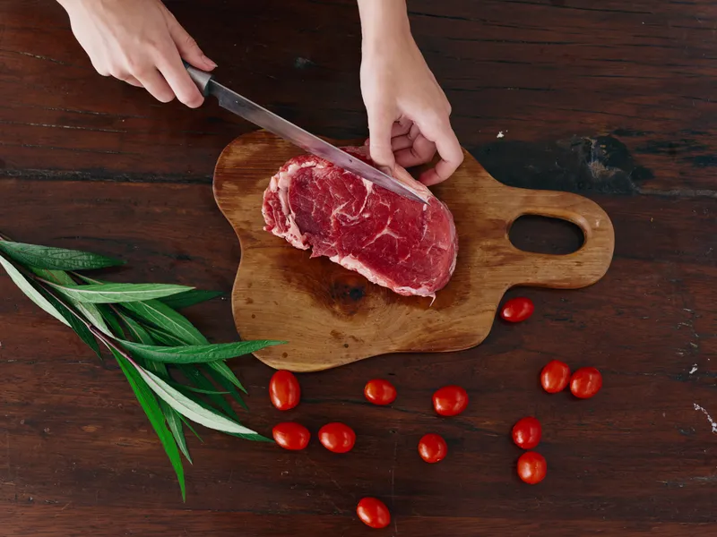 Женщина с ножом в руке нарезает свежее мясо для жарки на кухне