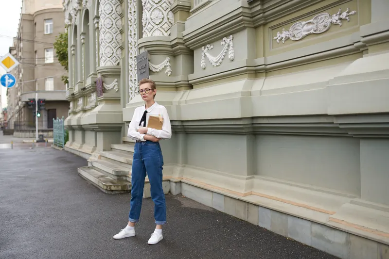 Симпатичная студентка с книгой в руке, в очках, на фоне старинного здания образовательного института