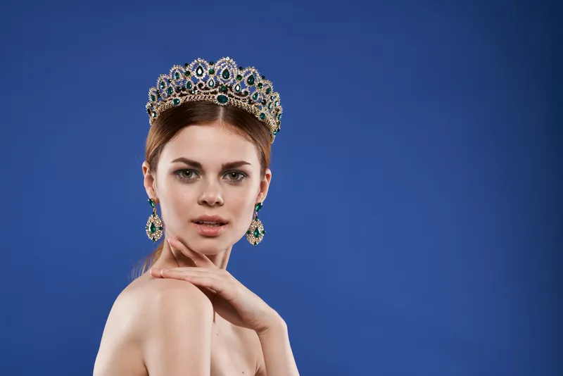 Портрет женщины в короне на голове, модель с макияжем, жест рукой на изолированном фоне