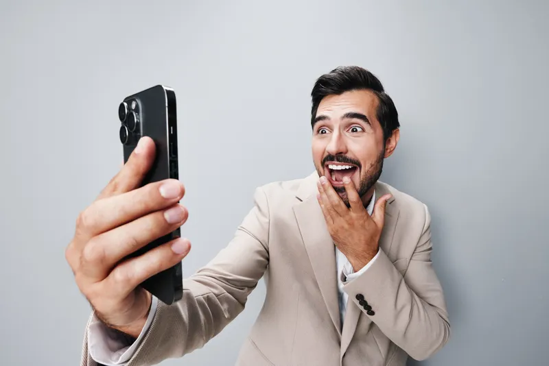 Уверенный и улыбающийся бизнесмен в деловом костюме держит смартфон и разговаривает по нему
