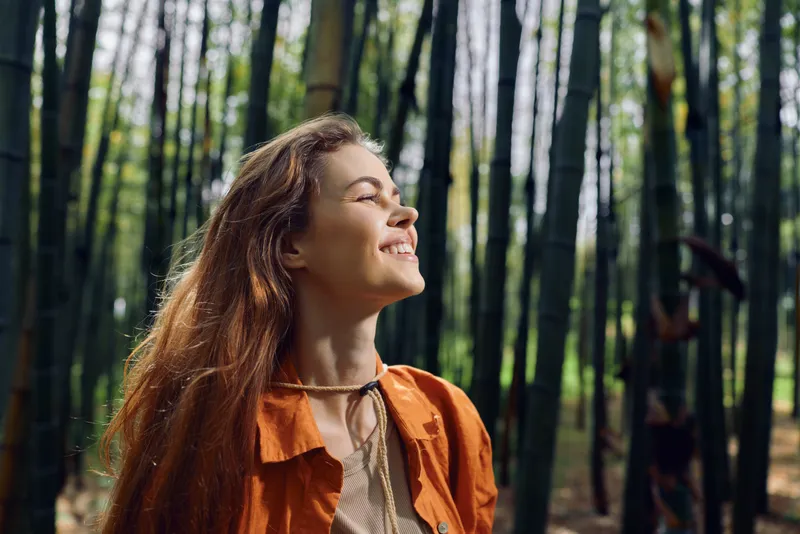 Woman smile forest bamboo nature portrait with sunlight and peaceful expression, young female enjoying outdoor relaxation, serene travel moment and green foliage atmosphere.