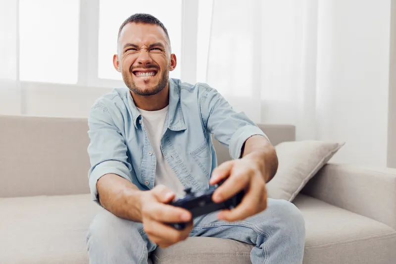 Happy man playing video games at home with excitement, showcasing modern lifestyle and entertainment trends, perfect for gaming and leisure themes.