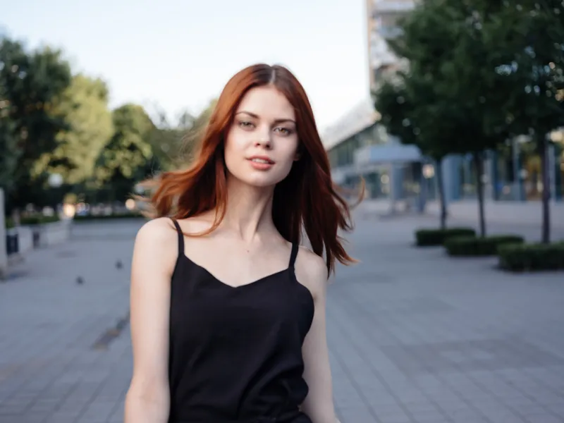 Модная женщина в черном платье идет по улице в парке на природе