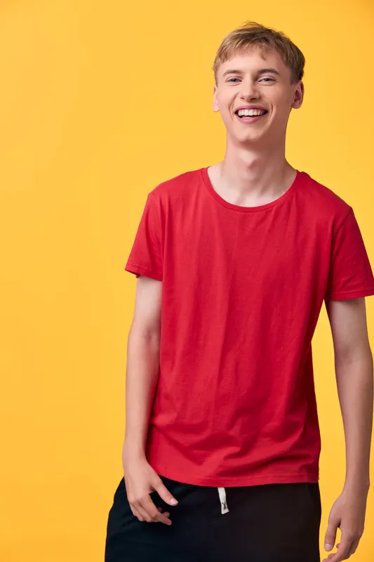 Smiling man in a red t shirt poses against a bright yellow backdrop, showcasing casual fashion and upbeat mood, ideal for lifestyle, youth culture, studio photography, and vibrant contemporary