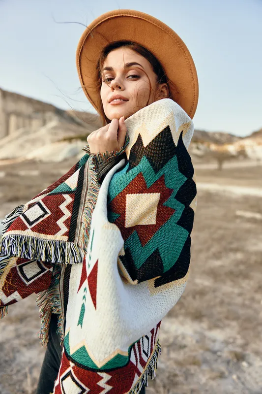 Женщина в шляпе и разноцветном одеяле стоит одна в бескрайнем пустынном пейзаже под ясным голубым небом