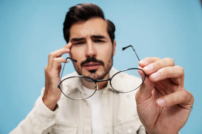 Крупный план портрета брюнета, который смотрит сквозь очки, которые держит в руках