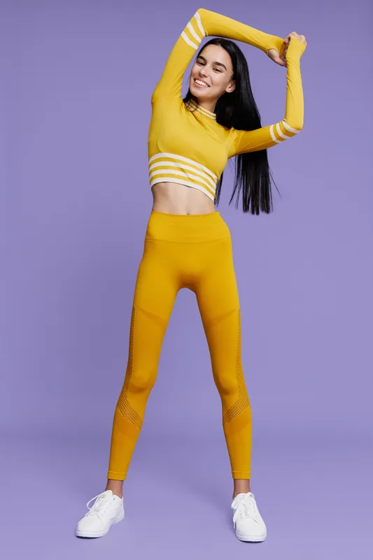 Woman sport fitness stretching in yellow activewear with long sleeves and leggings on purple background, smiling, healthy lifestyle, energy, exercise motivation.