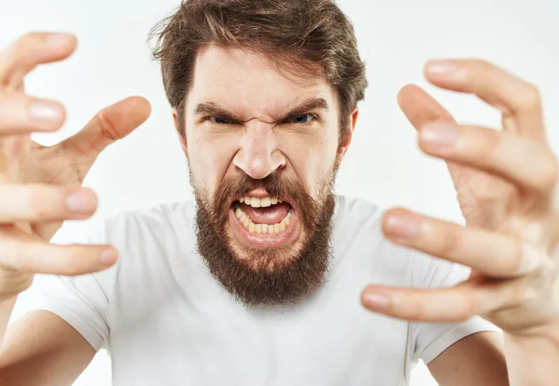 Молодой человек в белой футболке жестикулирует руками, выражая эмоции раздражительности и стресса