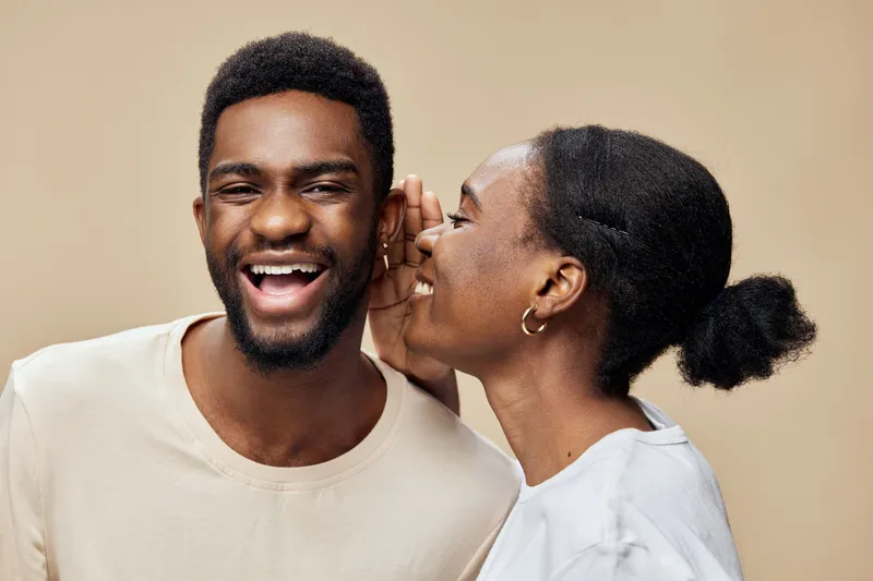 Joyful couple sharing secrets, showcasing happiness and connection, with a neutral background and warm tones for emotional engagement