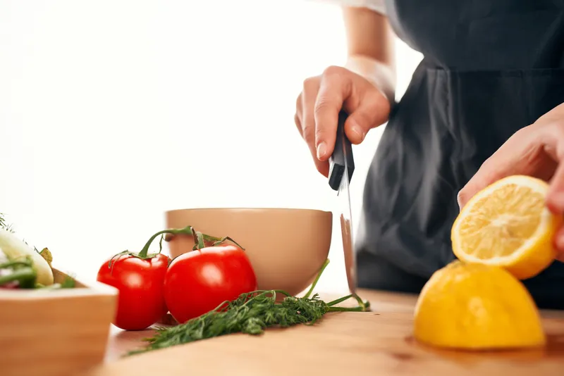 Шеф-повар с ножом в руках нарезает овощи и лимон, домашняя кухня
