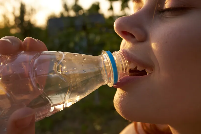 Крупный план лица женщины, пьющей воду из бутылки летом