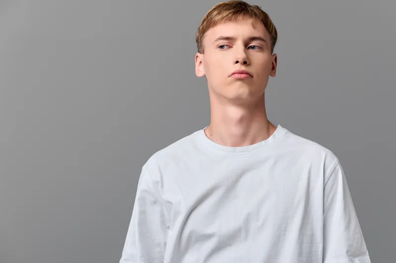 Young man, white t shirt, casual style, studio shot, neutral background, minimalist fashion, contemporary attitude, facial expression, creates a clean, modern image of everyday wear in a controlled