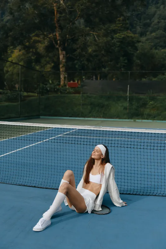 Young female tennis player in stylish sports attire relaxing by the court, showcasing athleticism and confidence in a vibrant outdoor setting