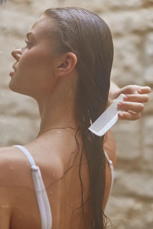 woman combing wet hair with white plastic comb, side profile, natural light, spa-like atmosphere, smooth skin, beauty and care concept, soft neutral background