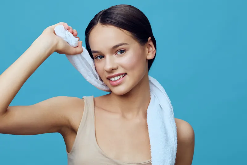 Young woman with a towel on her shoulder smiling against a blue background, showcasing healthy hair care and confidence in a vibrant and fresh style