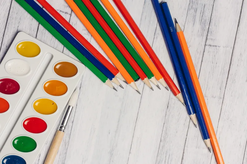 Яркие акварельные краски, стаканы и цветные карандаши на деревянном столе