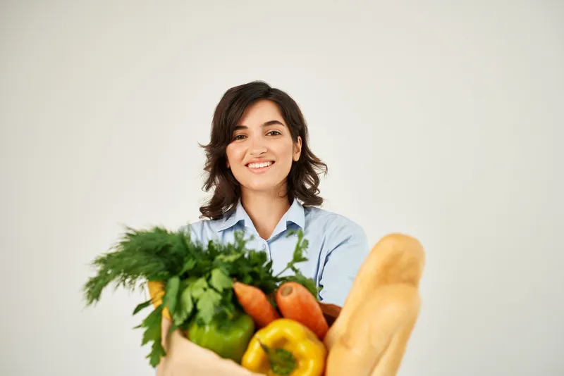 Милая брюнетка с пакетом продуктов на светлом фоне
