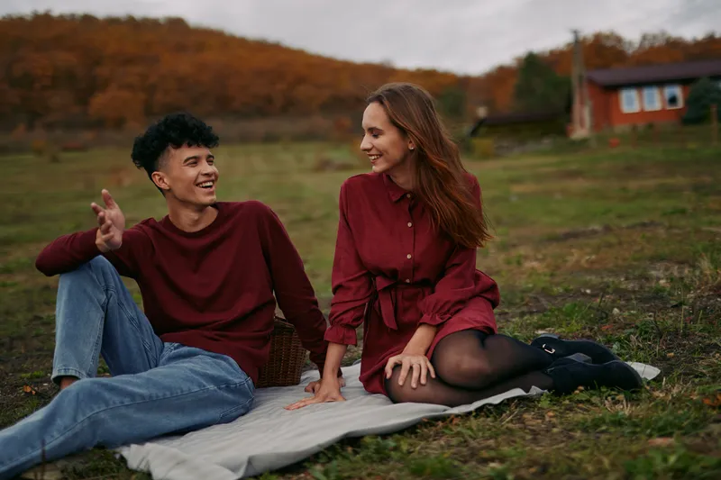 Authenticity and credibility shine in this moment as two people sit on a blanket in an autumn field, sharing easy laughter and a sincere connection.