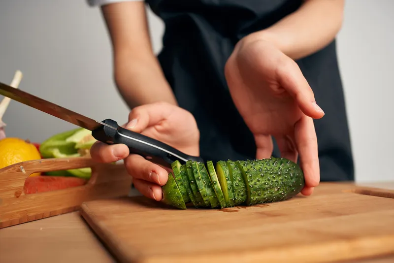 Женщина в черном фартуке нарезает овощи на кухне, домохозяйка готовит еду