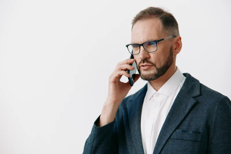 Business professional man on an isolated colorful background shows calm, focused emotion, conveying ambition and confidence through composed posture, thoughtful gaze, and firm phone conversation.