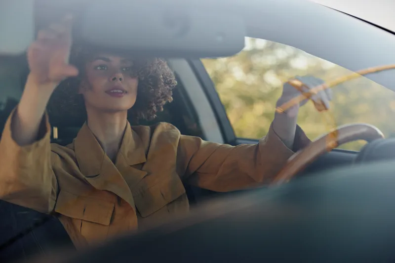 A stylish woman drives a car in a brown jacket, focused on the road. The retro film color adds warmth, evoking freedom, travel, and independent lifestyle.