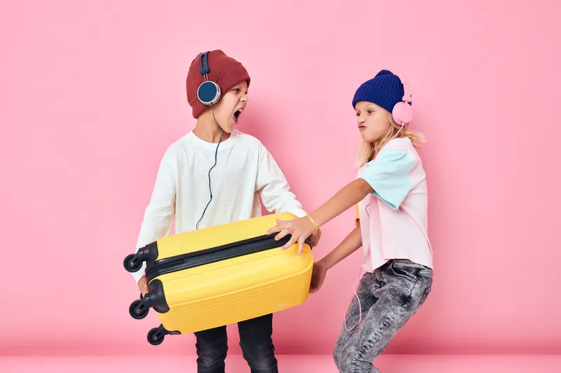 Забавные маленькие мальчик и девочка с жёлтым чемоданом и наушниками на изолированном фоне