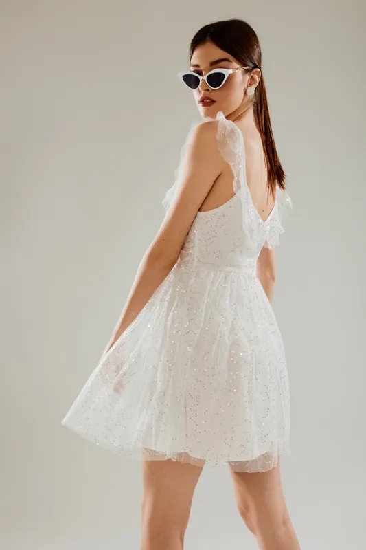 Young woman in a white lace dress and sunglasses poses sideways in a studio. Concept of woman beauty fashion with elegant style and modern accessories.