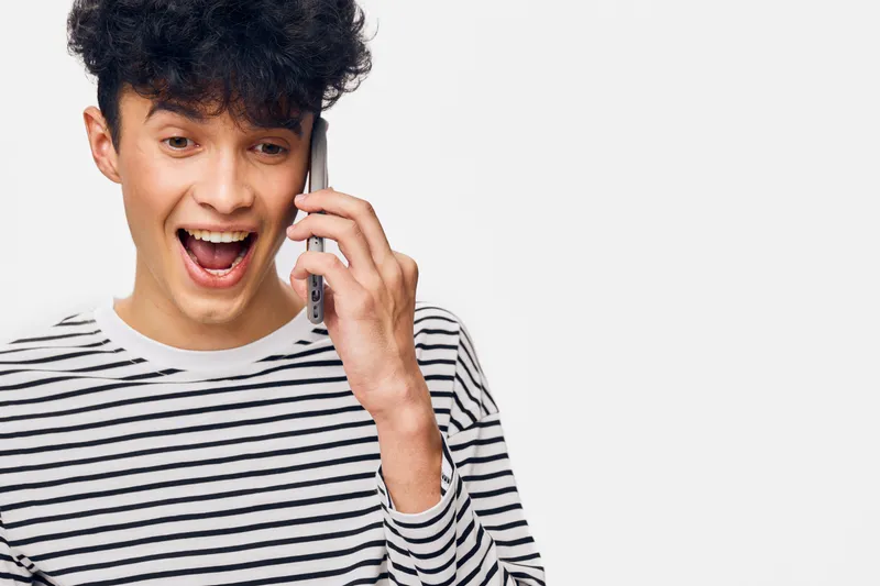excited man talking on smartphone with expression of surprise, wearing striped shirt against white background, modern casual style