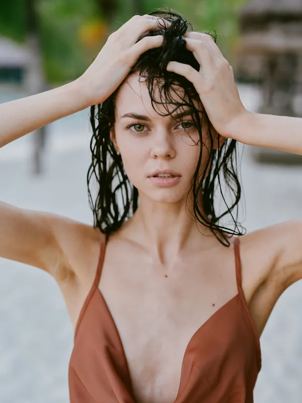 Closeup of a young woman with wet hair, bare shoulders, and a calm gaze, standing outdoors after a swim or rain, conveying vulnerability, strength, and natural beauty.