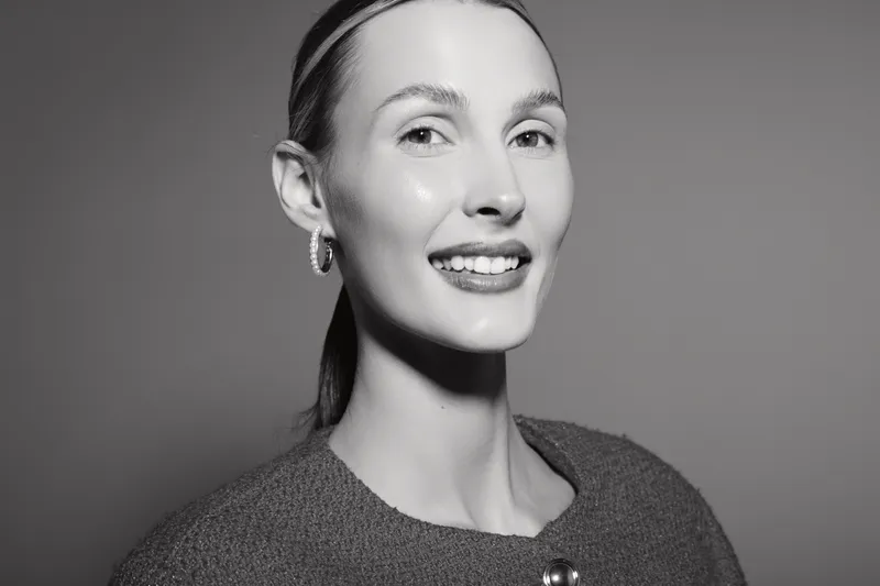 Smiling young Caucasian woman with fair skin and smooth hair poses in a dark sweater against a plain background. Concept for beauty, happiness, and natural portrait.