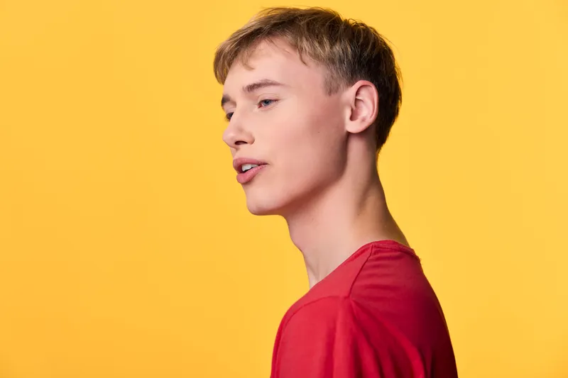Man in a red shirt shown in profile against a bold yellow backdrop, highlighting contemporary fashion and confident posture suitable for lifestyle and editorial stock imagery